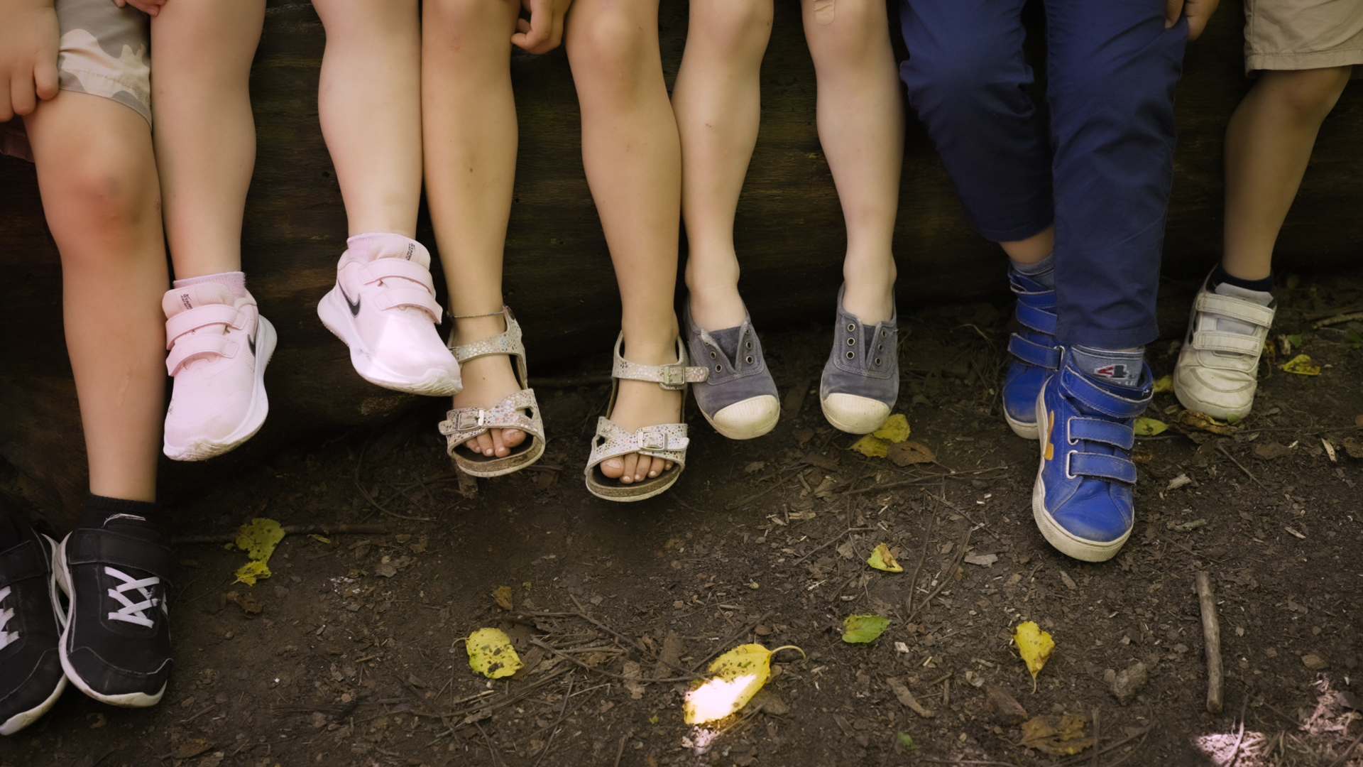 Sei bambini seduti su una panchina del parco della scuola montessoriana, si vedono solo le gambe dalle ginocchia in giù.