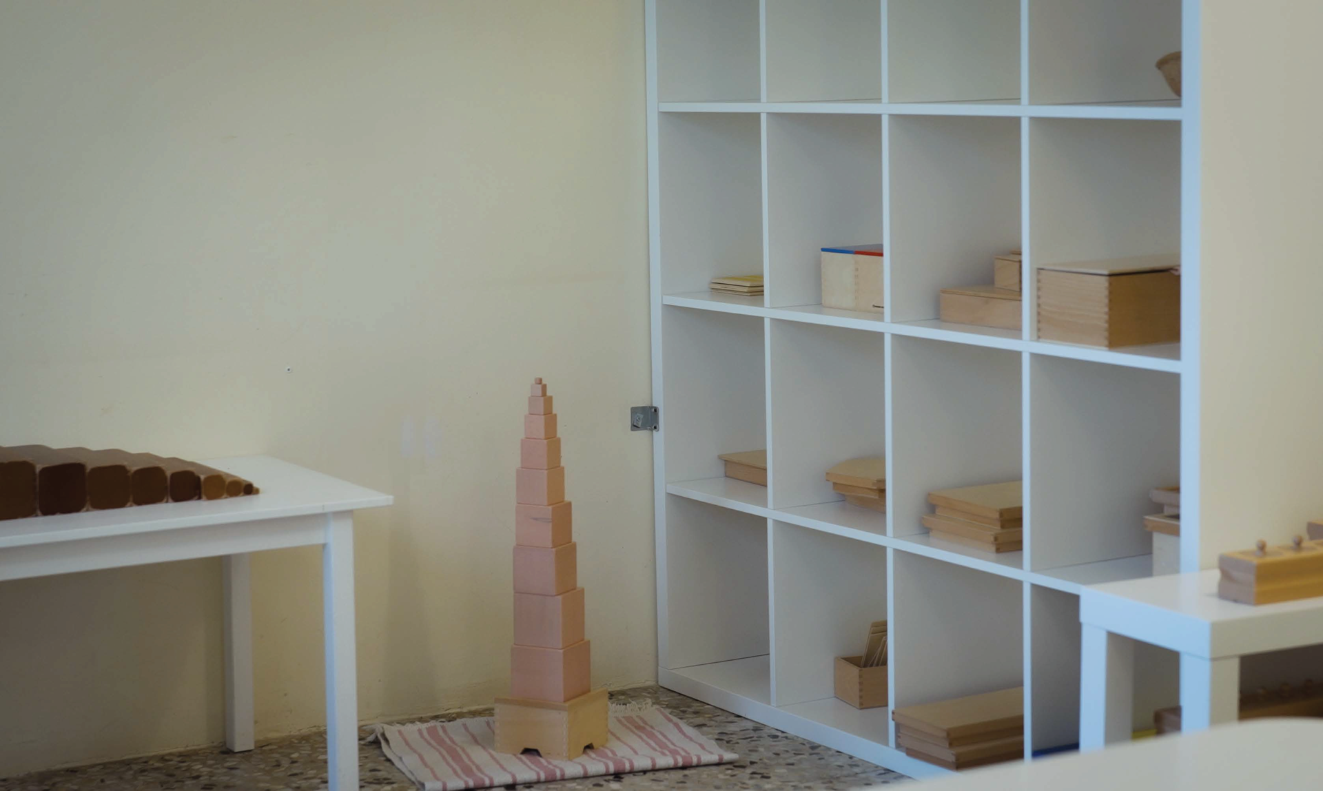 All’interno di un’aula, un mobile bianco in legno ospita i materiali del metodo Montessori, divisi in scomparti.